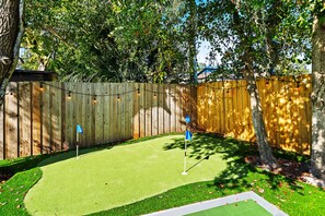 A backyard with a green artificial turf, a wooden fence, and a string of lights. - Private Resort w/ Heated Pool, Pickleball Court, Firepit... Near IMG and Beach! (Bradenton)