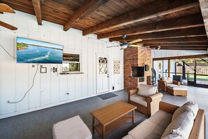 A spacious outdoor living area with a brick fireplace, wicker furniture, and a television mounted on the wall. - Private Resort w/ Heated Pool, Pickleball Court, Firepit... Near IMG and Beach! (Bradenton)