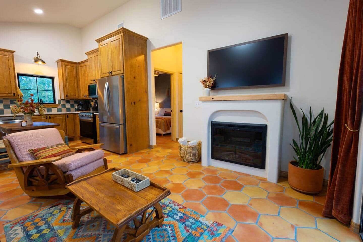 A modern kitchen with wooden cabinets and a built-in refrigerator, a cozy seating area with a patterned rug, and a fireplace with a mounted television above it.