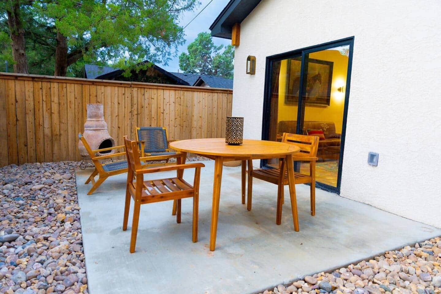 Een terras met een ronde tafel, vier houten stoelen, een barbecue en een houten omheining.