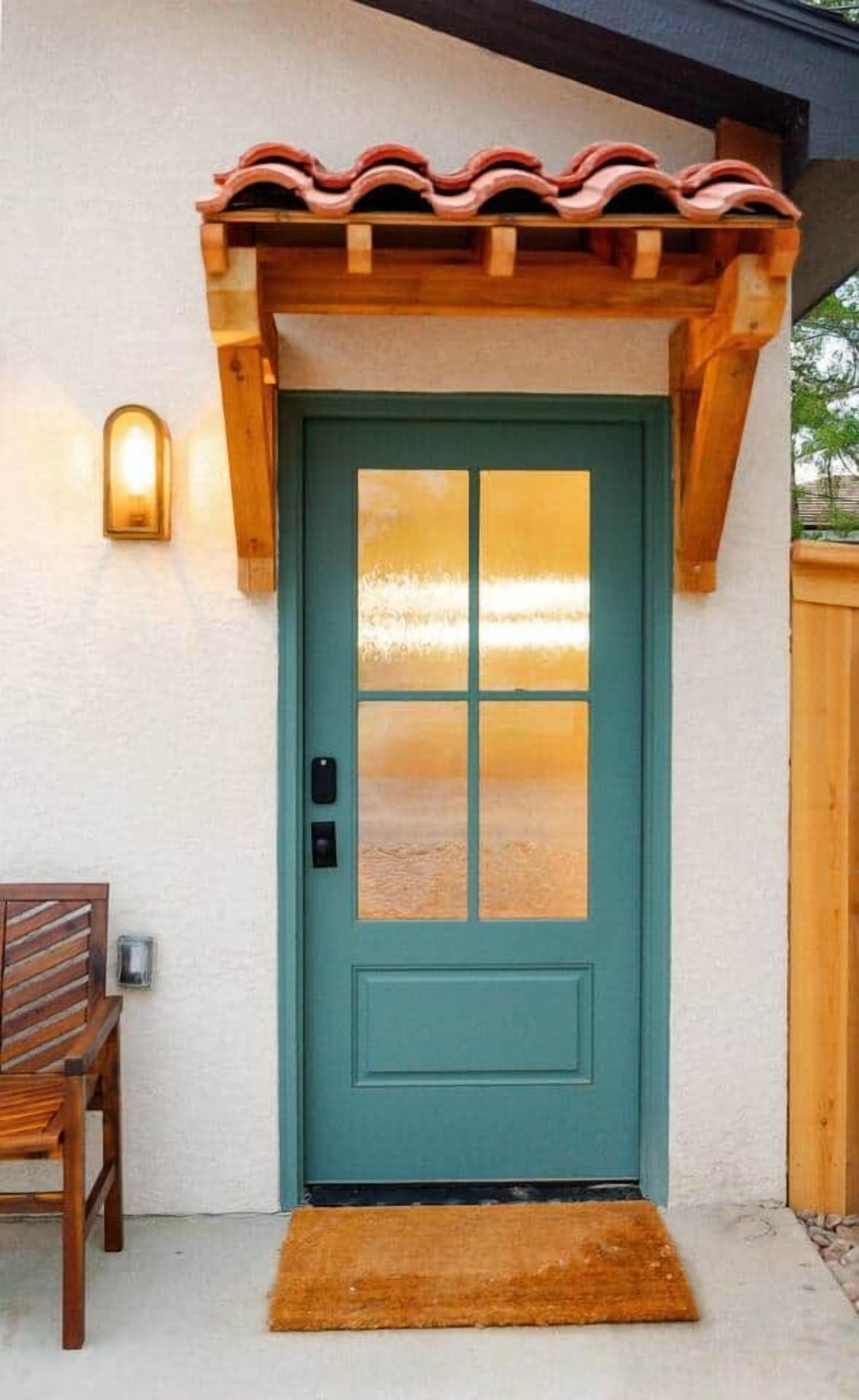 Een smaragdgroene deur met een ruit, een houten veranda met een pannendak, en een bank aan de linkerkant.