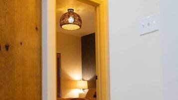 Un passadís amb una porta de fusta, una cistella de vimet i un llit amb una làmpada.