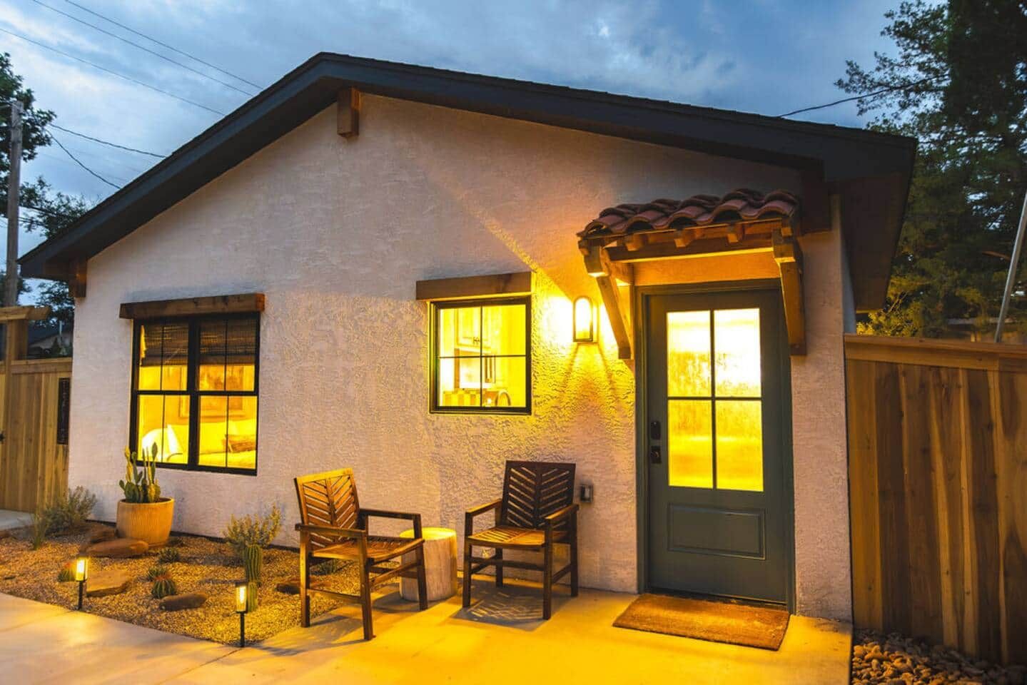 A two-story house with a front porch, two windows with lights, a door, and a small garden with a cactus.
