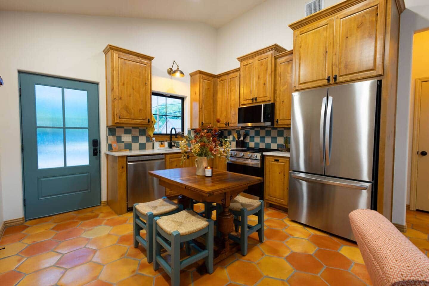 Una cocina con armarios de madera, un refrigerador de acero inoxidable, una estufa y un salpicadero a cuadros.