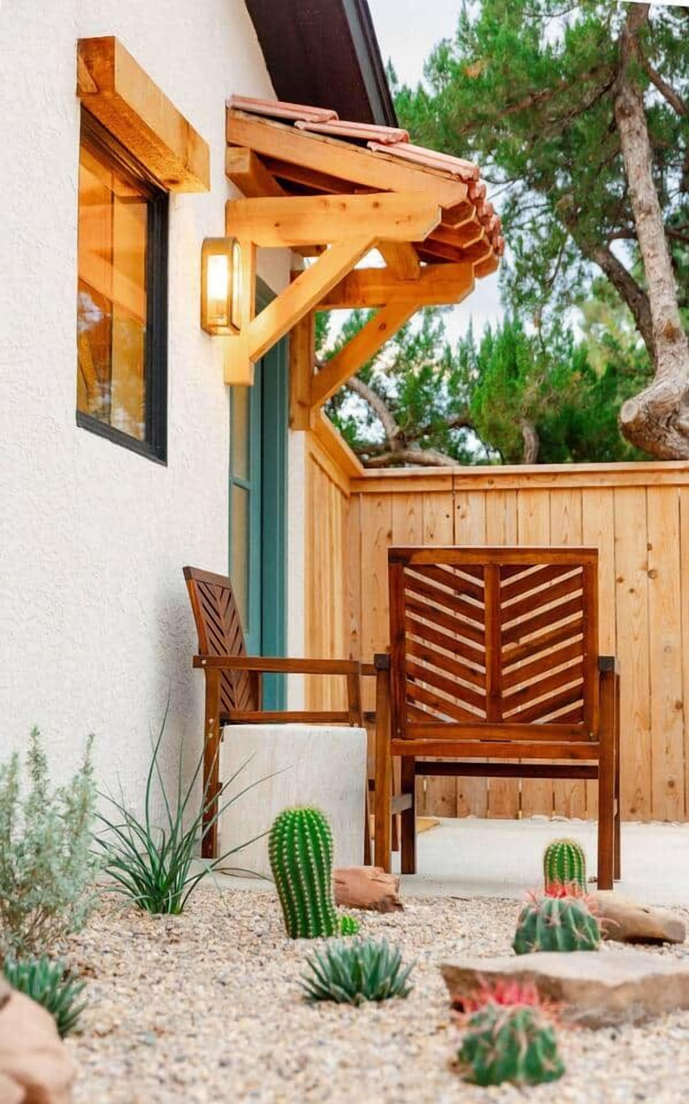Une pergola en bois avec une chaise et une table, une clôture en bois et des cactus dans un espace jardin.