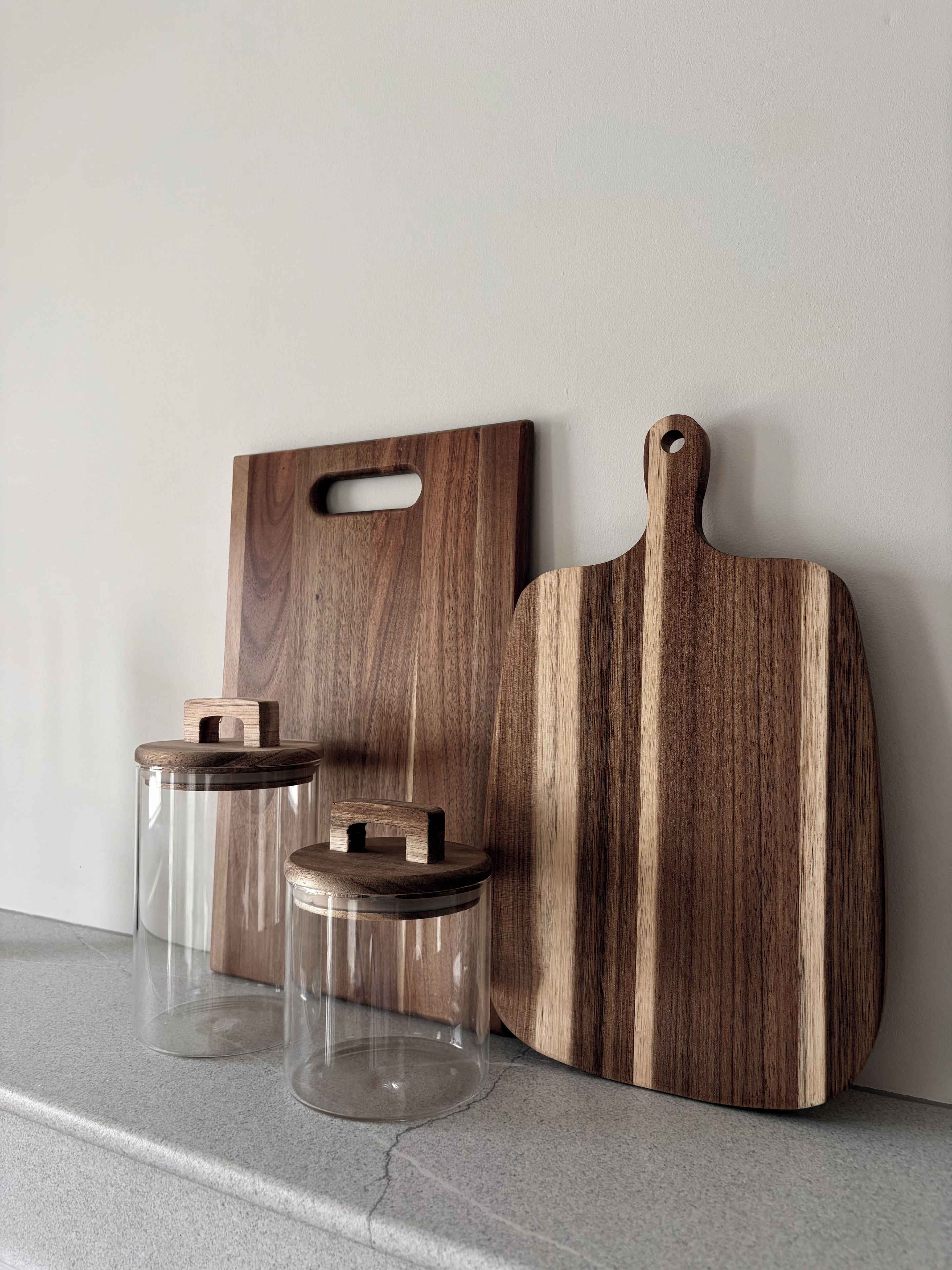 Una encimera de cocina con dos tablas de cortar de madera y dos tarros de vidrio con tapa.
