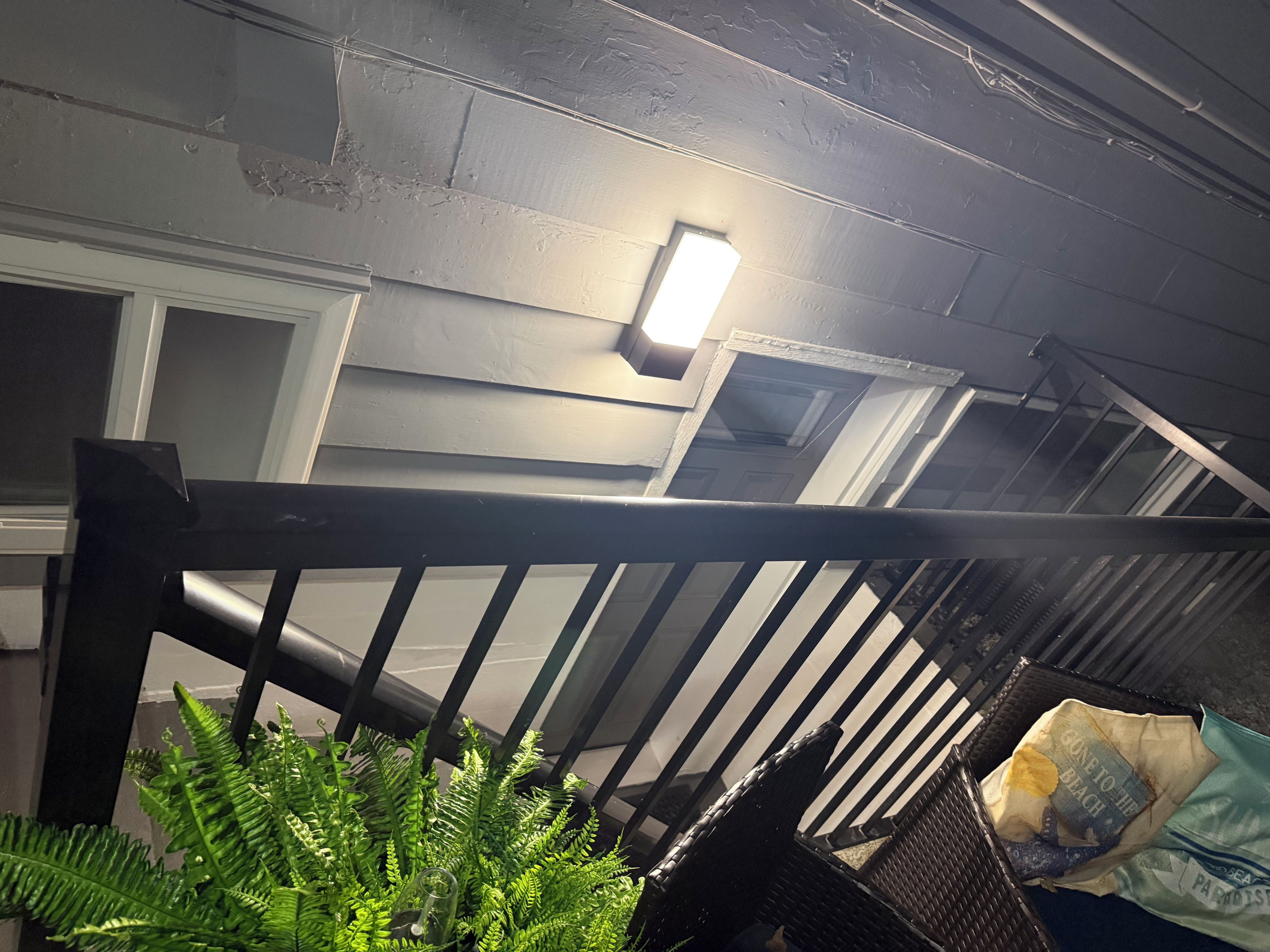 A staircase with a metal railing, a light fixture on the wall, and a bag of chips on the floor.