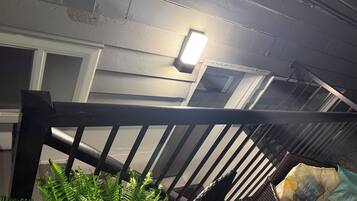A staircase with a metal railing, a light fixture on the wall, and a bag of chips on the floor.