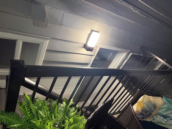 Una escalera con barandilla de metal, una lámpara en la pared y una bolsa de papas en el suelo.