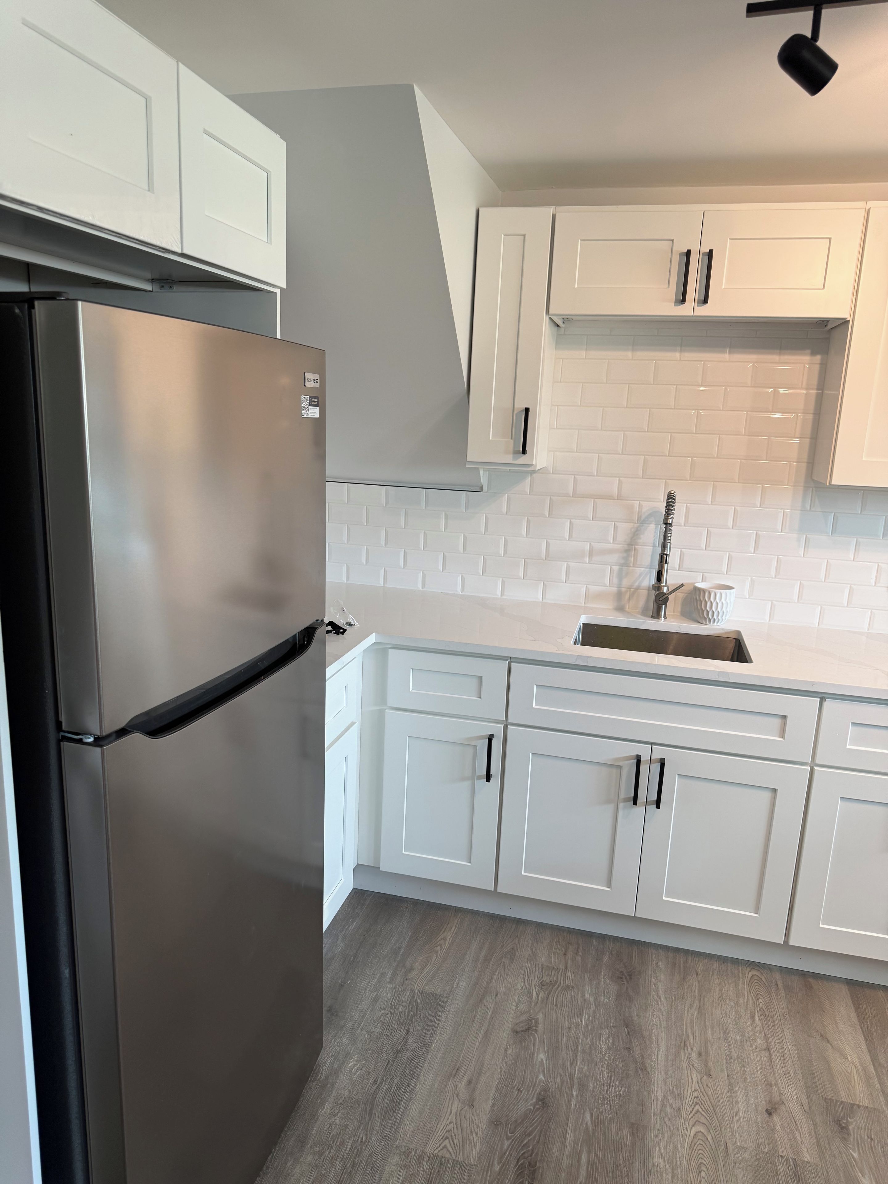 A kitchen with white cabinets, a stainless steel refrigerator, and a tiled backsplash.