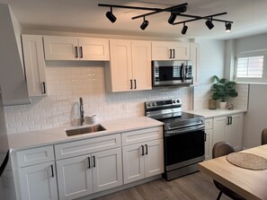 Una cocina moderna con armarios blancos, electrodomésticos de acero inoxidable y una zona de comedor con mesa de madera.