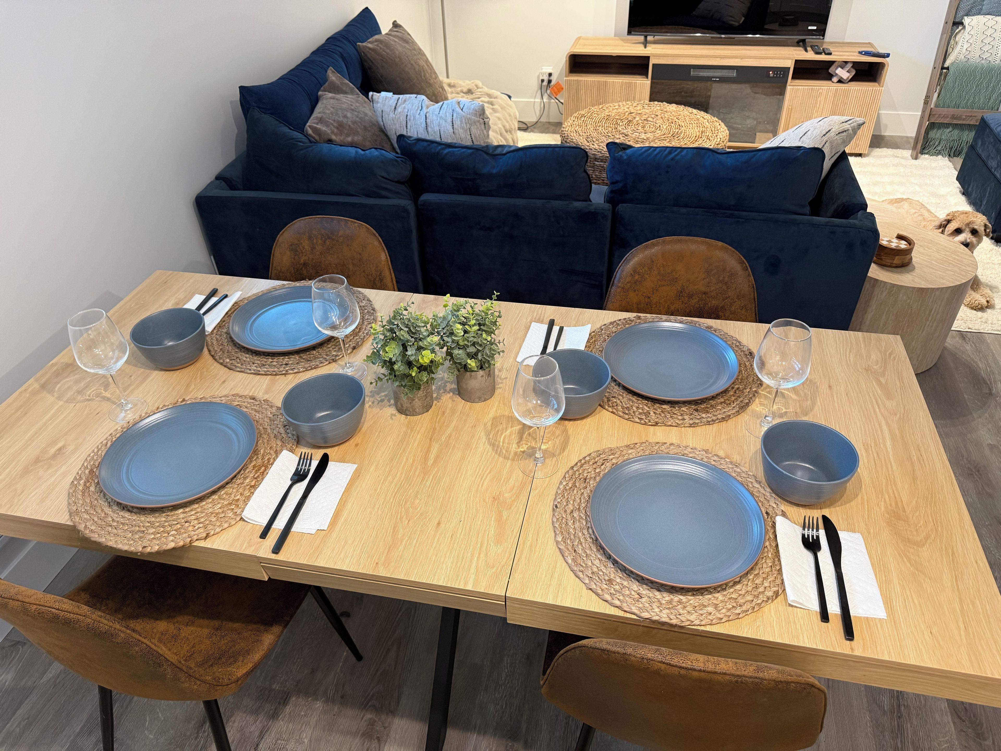 A dining table set with plates, bowls, glasses, and cutlery, surrounded by chairs.