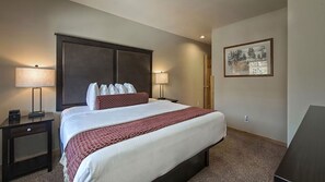 A hotel room with a large bed, two bedside tables, a nightstand, a lamp, a framed picture on the wall, and a door. - Ski-In/Ski-Out Spacious 1BR Condo at Grand Timber Lodge, Sleeps 4 (Breckenridge)