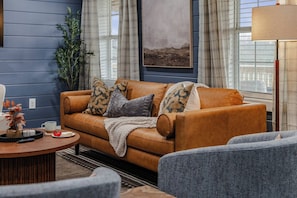 A cozy living room with a brown leather sofa, a coffee table, and a blue armchair. - Prather Ridge Estate | 3BR | Bourbon + Pickleball + Sauna (Chaplin)