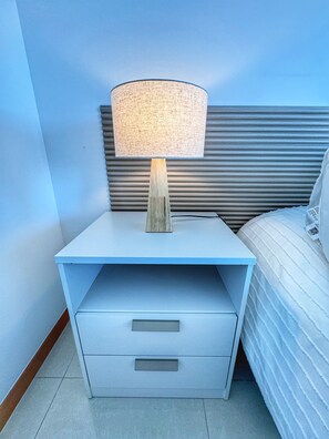 A nightstand with a lamp, a drawer, and a bed with a striped pillow. - High-Floor 1-Bedroom Apartment with City Views | Tressesenta Tower (Punta del Este)