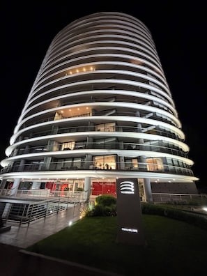 A multi-story hotel with a curved facade, illuminated windows, and a sign indicating 'TRESSENTA' and 'PUNTA DEL ESTE'. - High-Floor 1-Bedroom Apartment with City Views | Tressesenta Tower (Punta del Este)