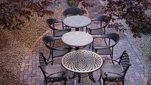 Un espace patio avec une table ronde et six chaises, entouré d’un chemin en briques.