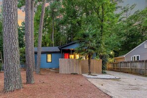A small cabin with a wooden deck, surrounded by trees and a gravel driveway. - Outdoorsy, Sauna, Ice Bath, Pets OK, 10 min Dtwn (Raleigh)