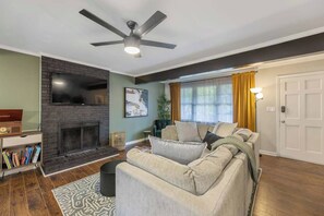 A living room with a fireplace, a sofa set, a ceiling fan, and a television. - Outdoorsy, Sauna, Ice Bath, Pets OK, 10 min Dtwn (Raleigh)