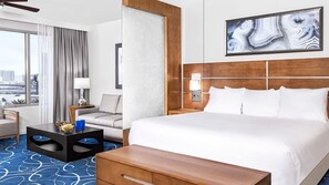 Habitación de hotel con cama, escritorio, silla, lámpara y un cuadro en la pared.