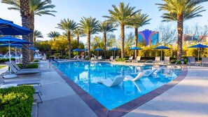 A pool area with lounge chairs and umbrellas, surrounded by palm trees.