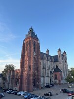 Una iglesia grande con una torre destacada, un estacionamiento con coches, y un cielo azul despejado.