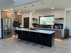A modern kitchen with a large island, stainless steel appliances, and pendant lighting. - Roundup Lodge 5 Bedrooms All w Private En-Suites No-Steps No-gravel LuxAmenities (Lead)