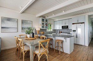 Une cuisine avec des meubles blancs, un îlot central doté de tabourets et une table à manger avec des chaises.