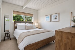 A bedroom with a wooden bed, a bedside table with a lamp, a small stool, and two framed pictures on the wall. - 180º Ocean View Summerland Retreat • 3 BR + 2 Decks + Backyard (Summerland)
