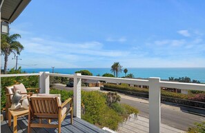 A wooden deck with chairs overlooking a road and ocean view. - 180º Ocean View Summerland Retreat • 3 BR + 2 Decks + Backyard (Summerland)