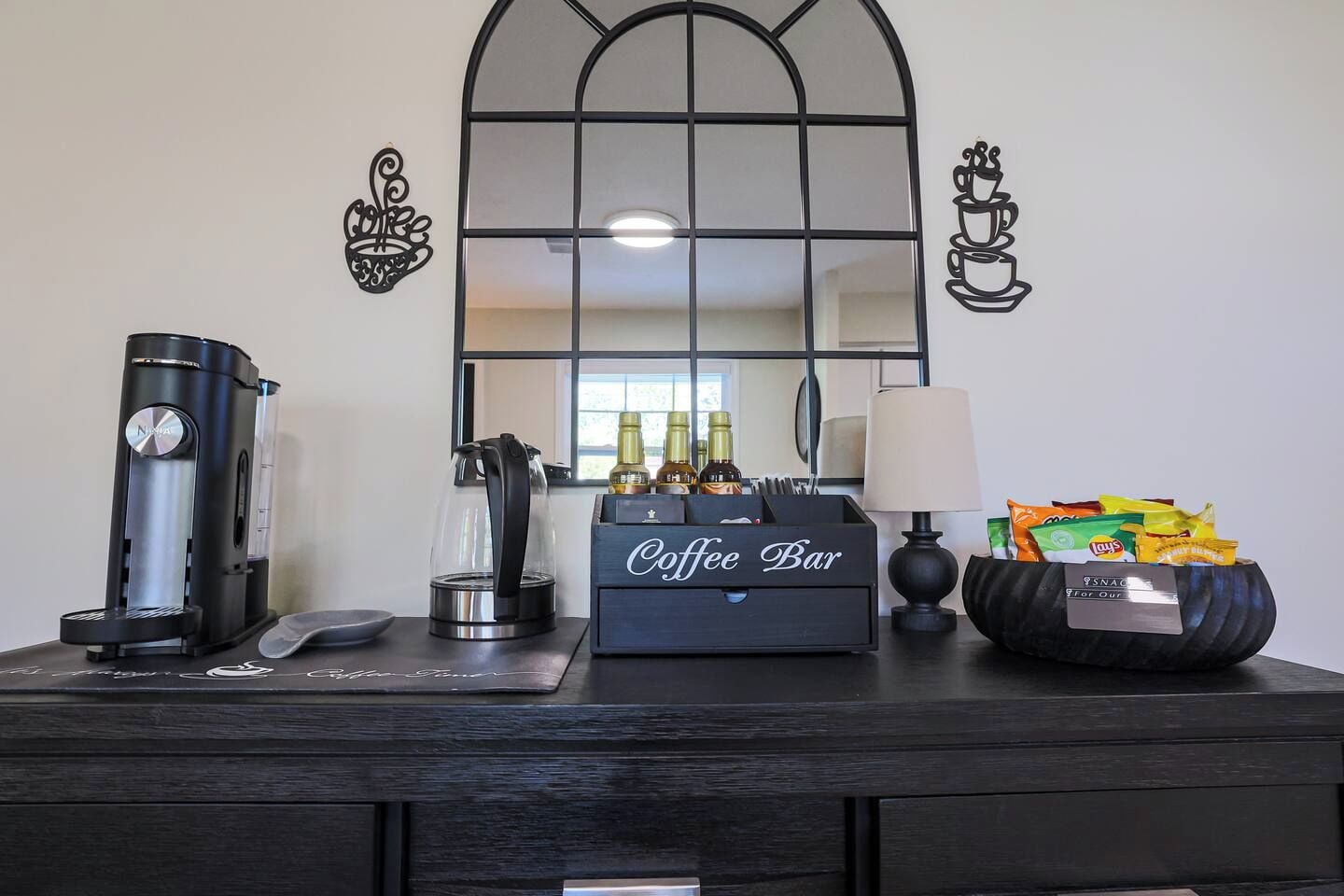 A coffee station with a coffee maker, a kettle, a coffee bar, snacks, and a lamp.