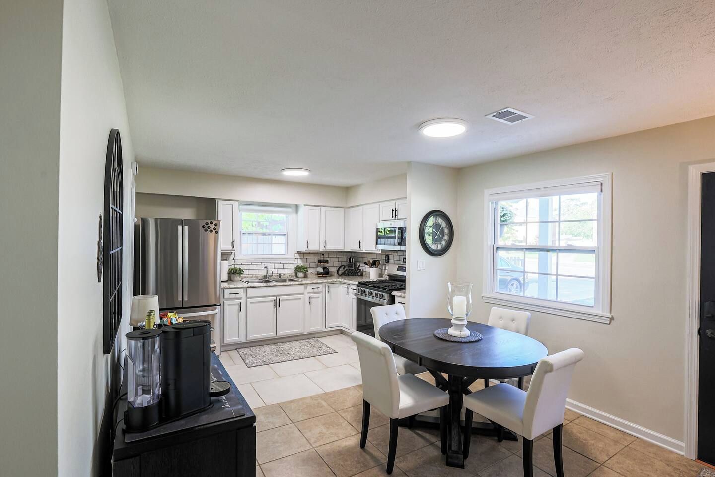 A modern kitchen with white cabinets, a dining area with a round table, and a clock on the wall.