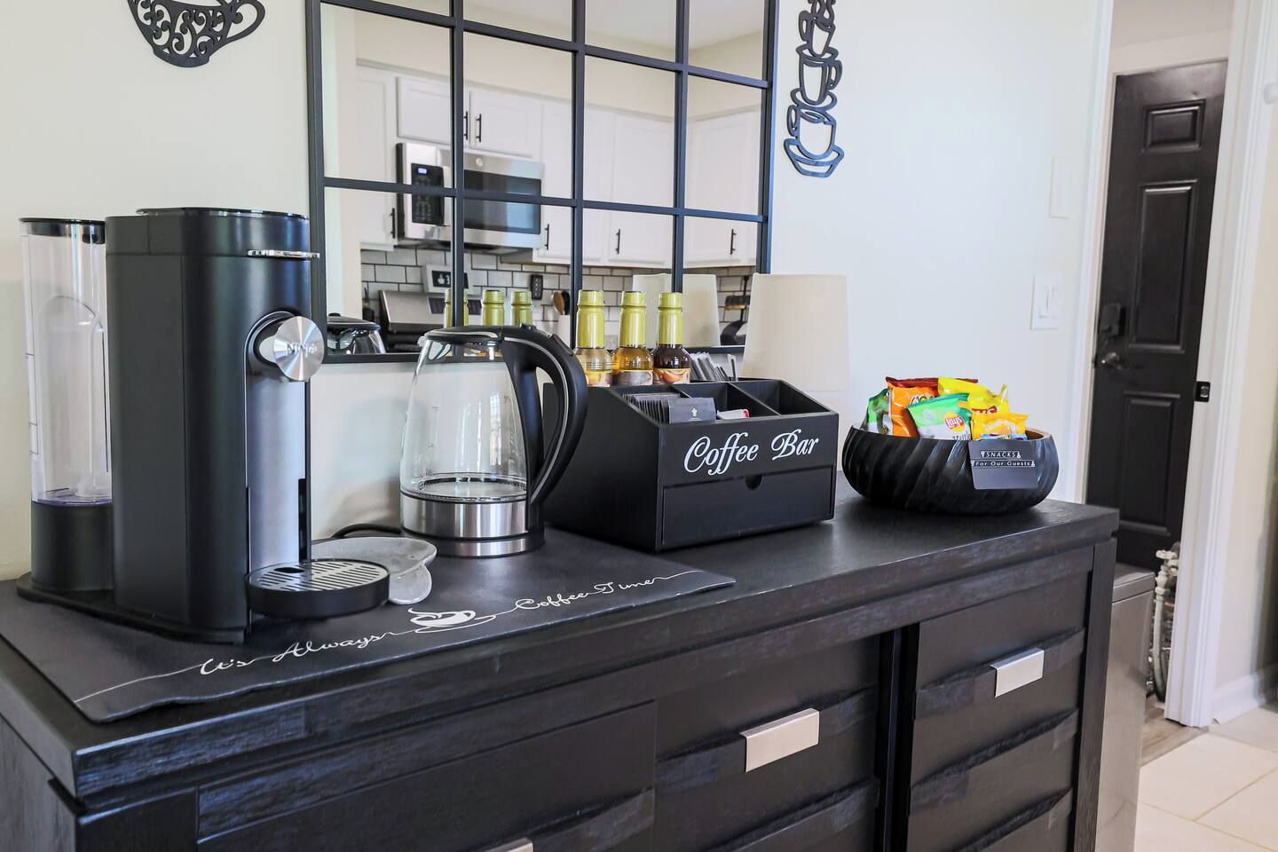 A coffee bar setup with a coffee maker, a glass carafe, a coffee pot, a coffee station, and a snack bowl.