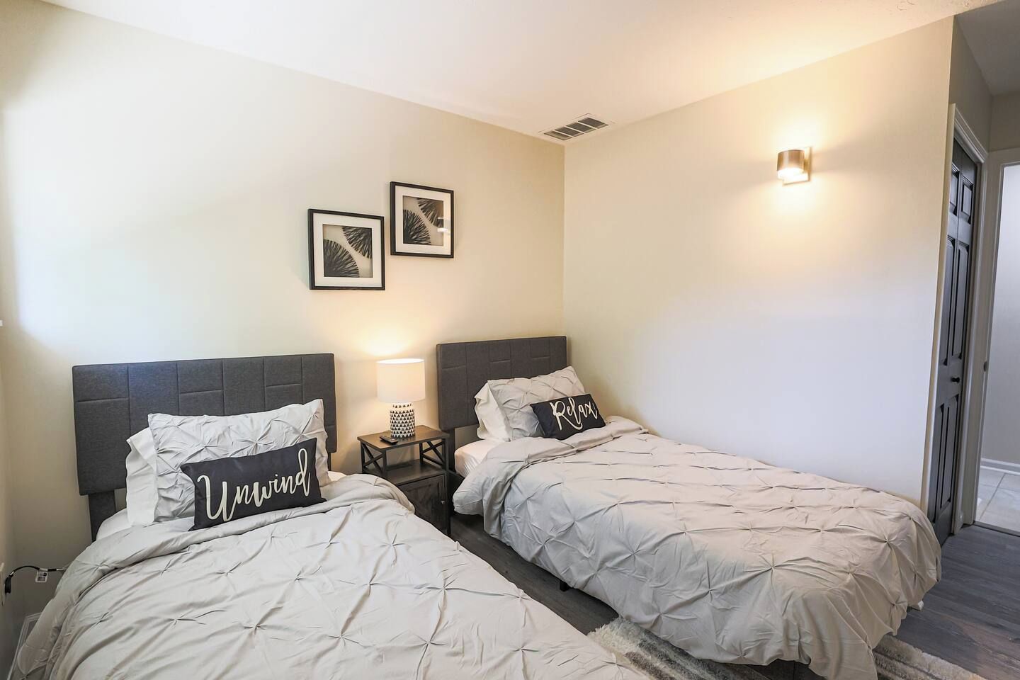 A hotel room with two beds, a nightstand with a lamp, and wall-mounted artwork.