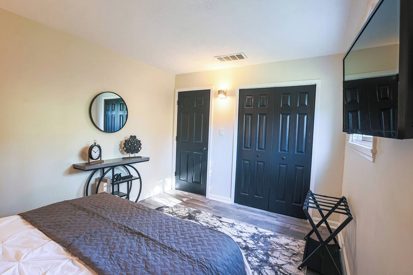 Une chambre à coucher avec un lit, un bureau avec une horloge, un miroir et deux portes.