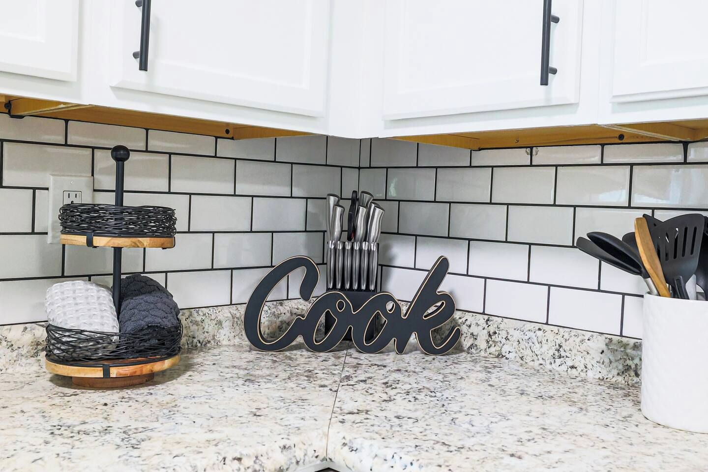 A kitchen with white cabinets, a tiled backsplash, and a 'Cook' sign.