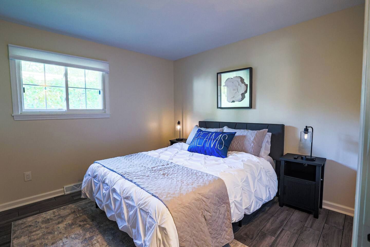 A bedroom with a bed, a nightstand, a wall-mounted lamp, and a window.
