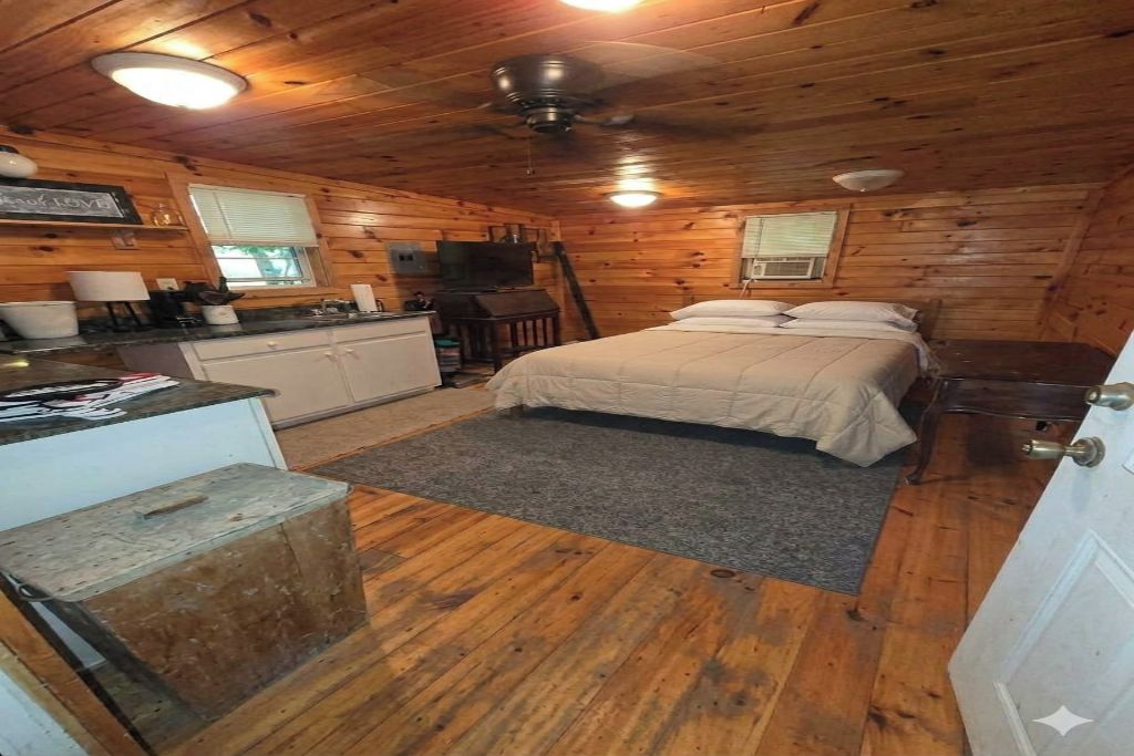 A cabin interior with a bed, kitchenette, and a ceiling fan.