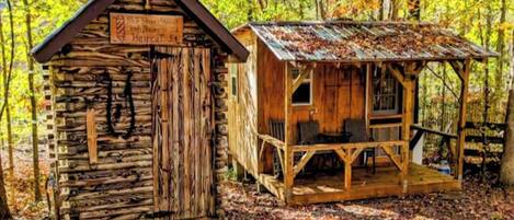 Una cabaña rústica con fachada de madera y un porche, rodeada de bosque.