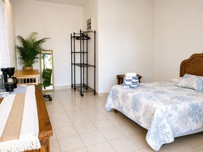 A bedroom with a bed, a bedside table, a chair, a coffee table, a plant, a shelf, and a window. - Best Ocean View and Pool (San José del Cabo)