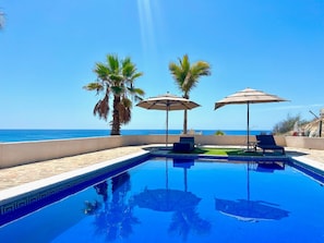 A swimming pool with two umbrellas, a lounge chair, and a view of the ocean. - Best Ocean View and Pool (San José del Cabo)