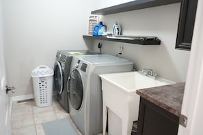 Un espace buanderie compact comprenant deux machines à laver, un évier blanc et une étagère avec des produits de lessive.