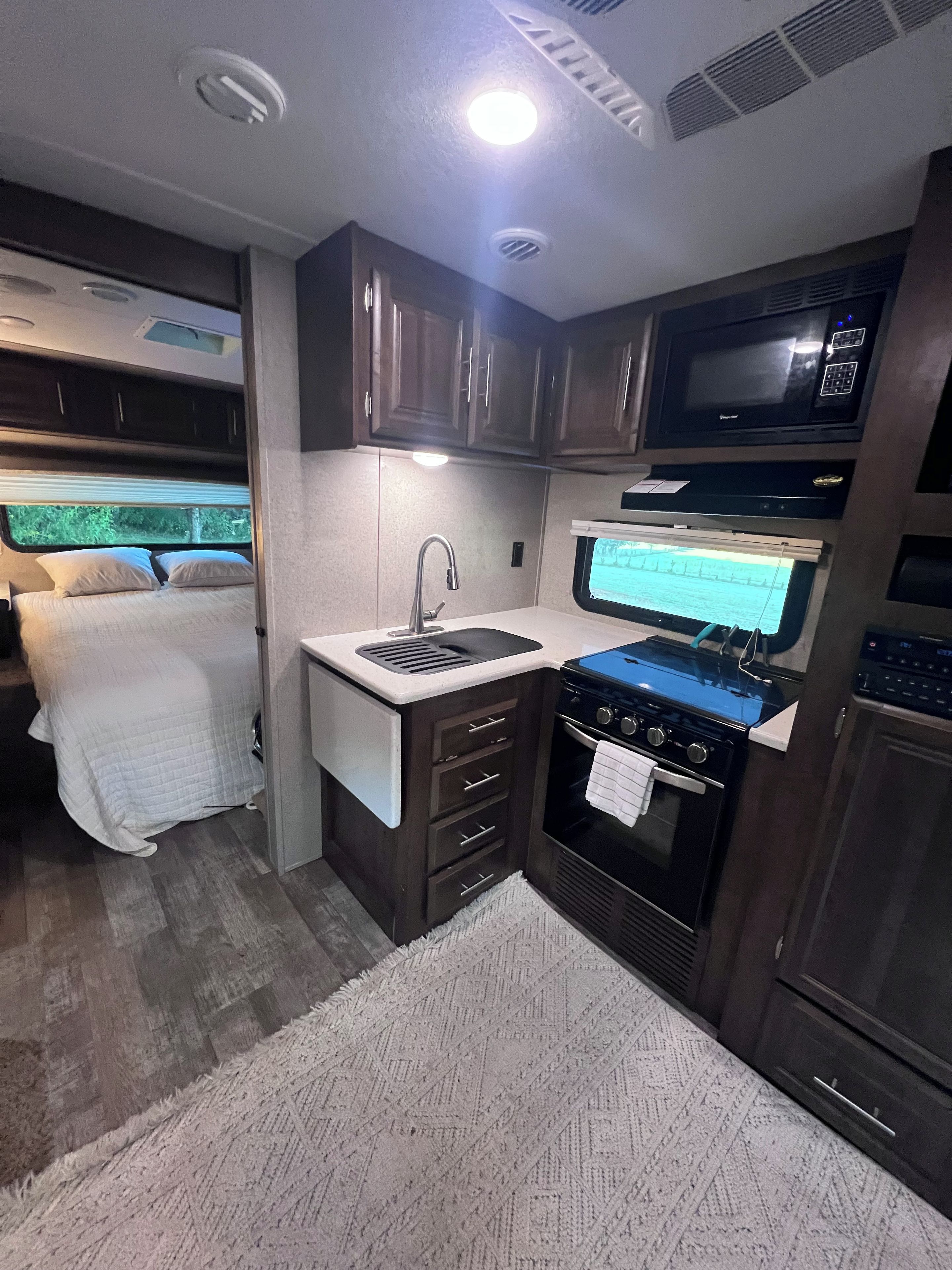 A compact RV kitchen with a stove, sink, and microwave.