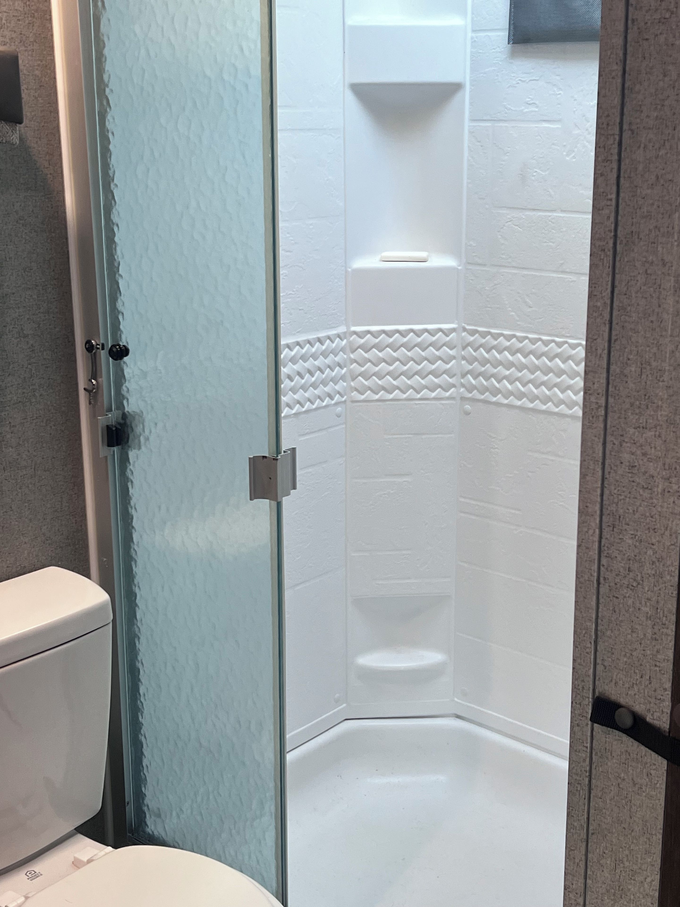 A corner shower with a glass door, white tiled walls, and a toilet visible to the left.