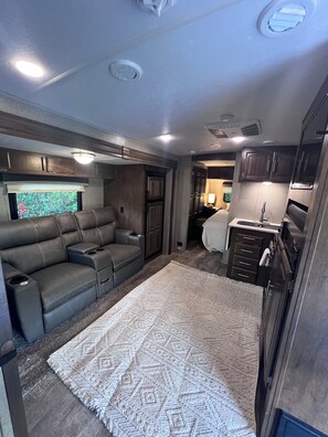 Un intérieur de camping-car compact comprenant un canapé, un coin cuisine et une fenêtre offrant une belle vue.