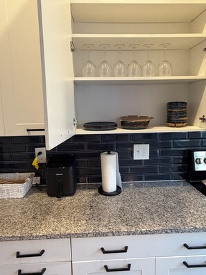 A kitchen with a black tiled backsplash, a countertop with a paper towel dispenser, a coffee maker, and a set of wine glasses on a shelf. - The Midnight Escape/Fast&Furious Suite (Atlanta)