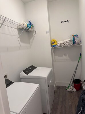 A laundry room with a washing machine, a dryer, shelves with cleaning supplies, and a mop. - The Midnight Escape/Fast&Furious Suite (Atlanta)