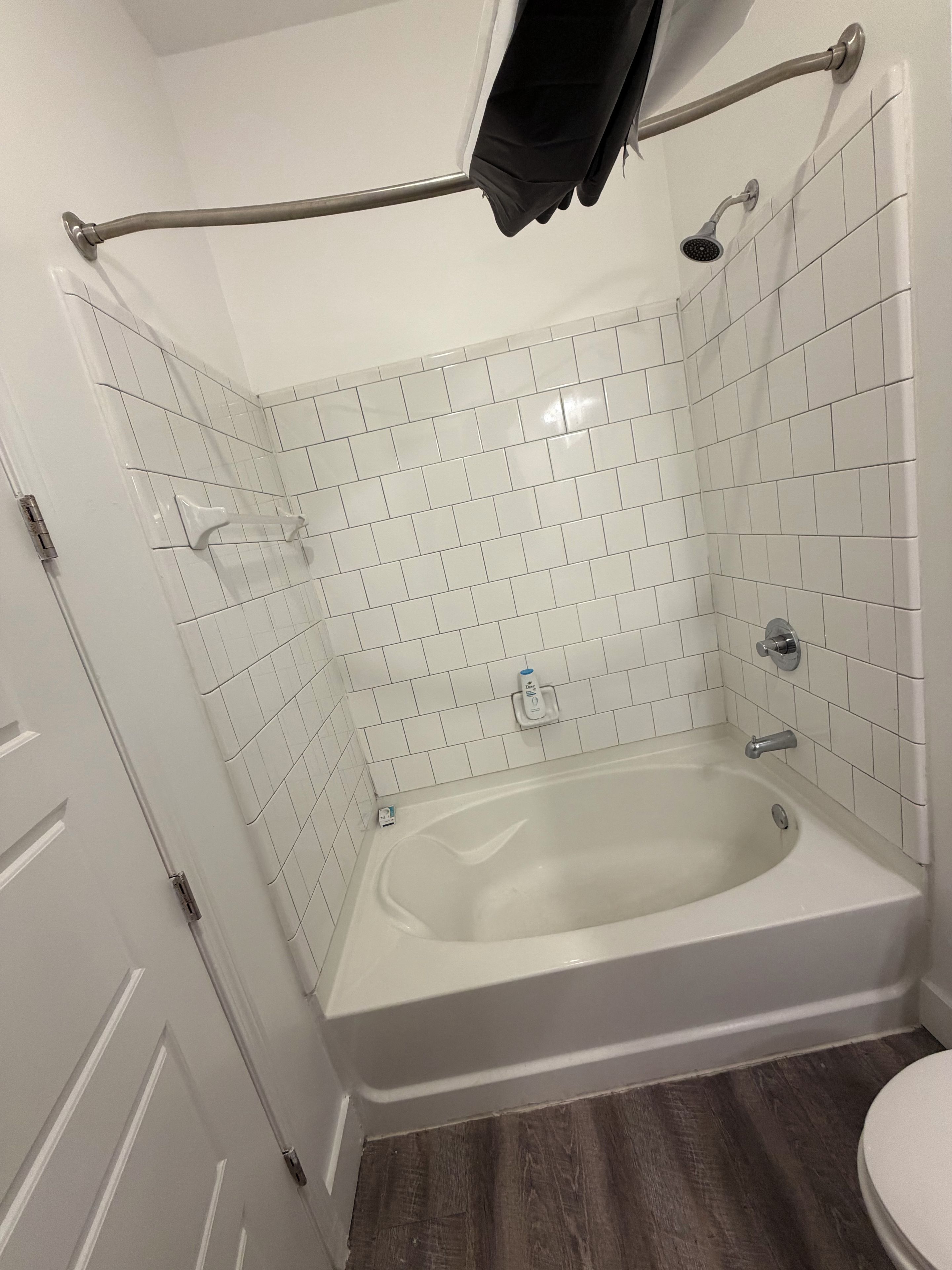 A bathroom with a corner bathtub, white tiled walls, a showerhead, and a towel rack.