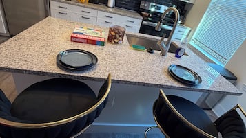 A kitchen with a granite countertop, stainless steel appliances, and two black bar stools.