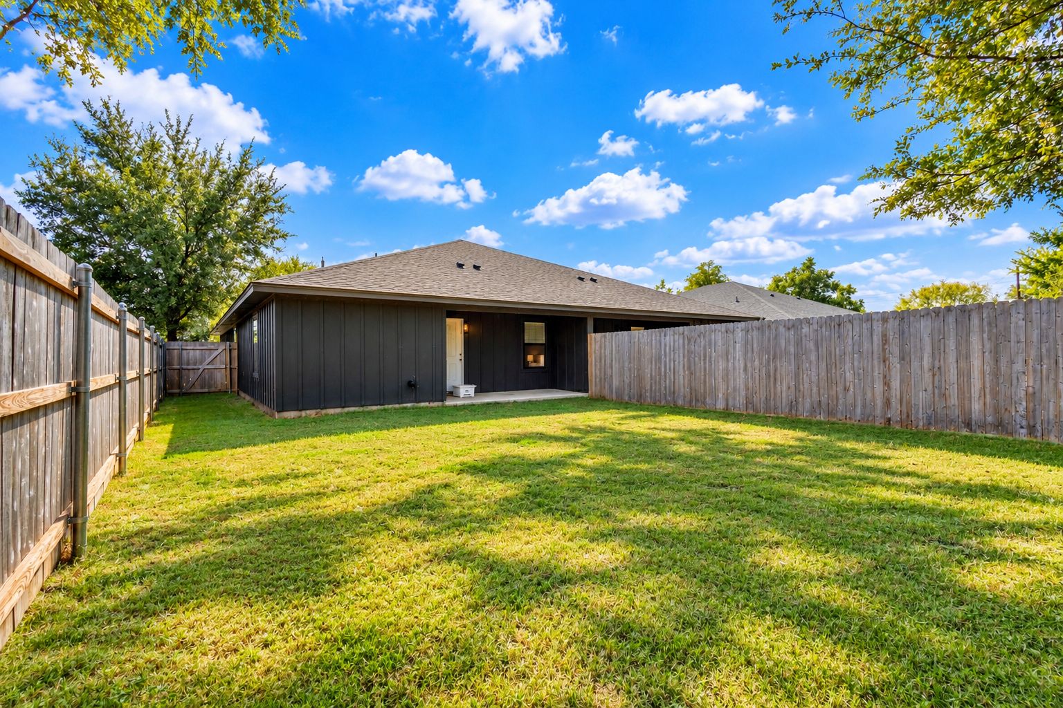A residential backyard with a house, a wooden fence, and a grassy lawn.